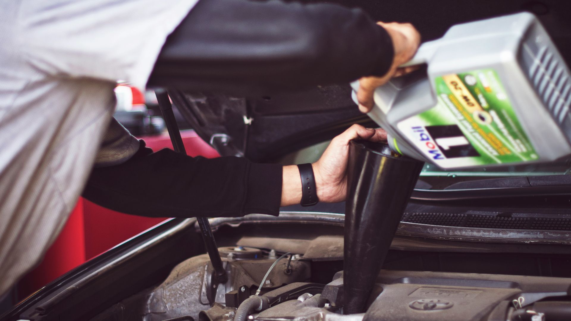 man refilling motor oil on car engine bay