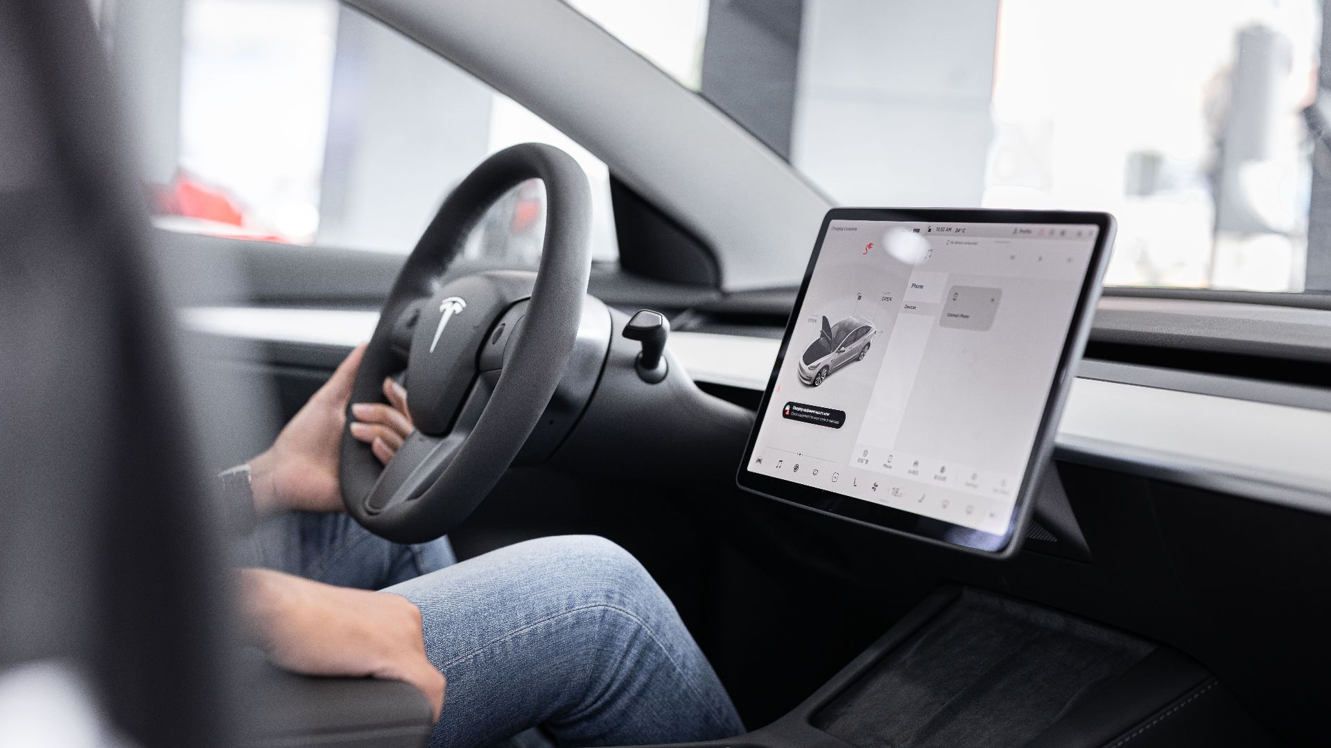 Interior of an electric car showing steering wheel and large touchscreen display, indicating modern technology.