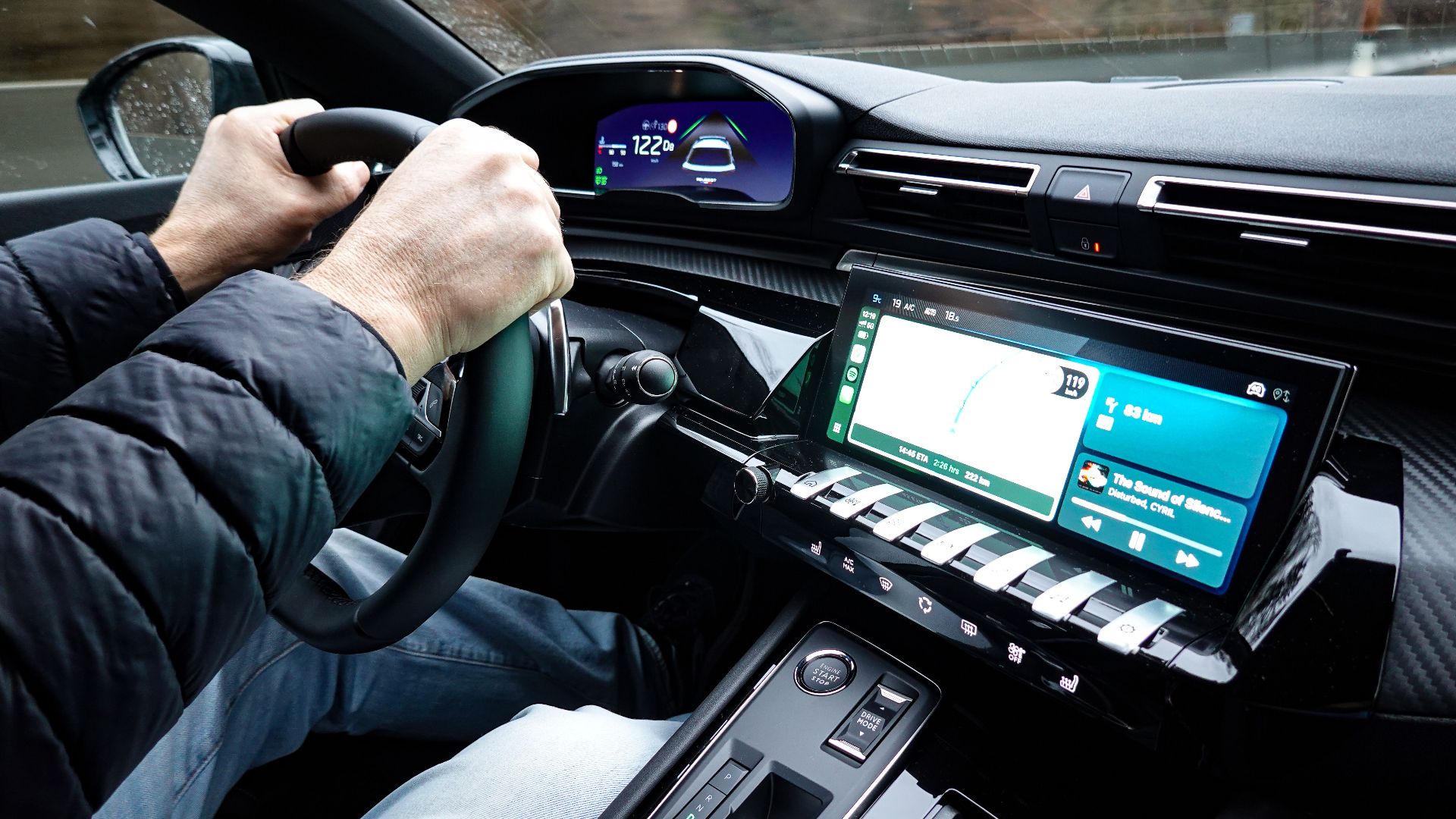 A detailed view of a car's interior with hands on the steering wheel, showcasing modern technology.
