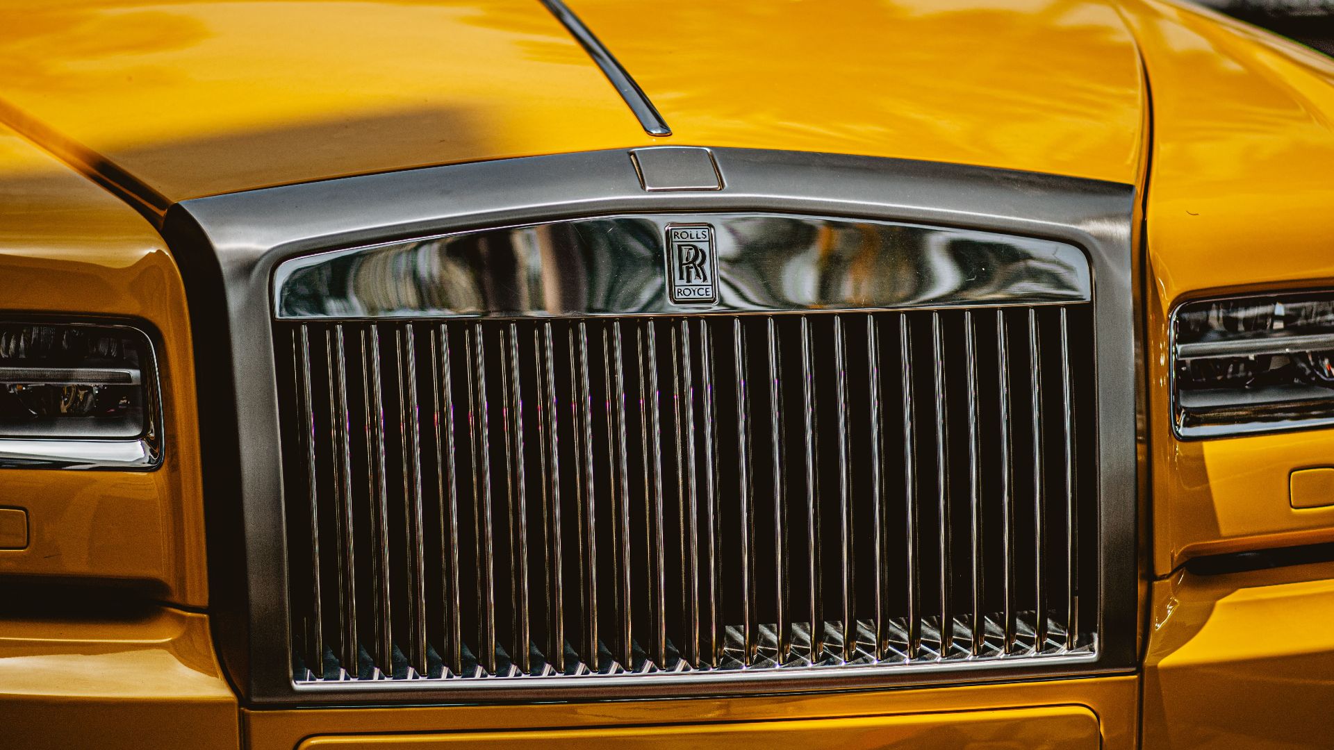 Detailed close-up of a luxury yellow car's front grille showcasing its iconic design elements.
