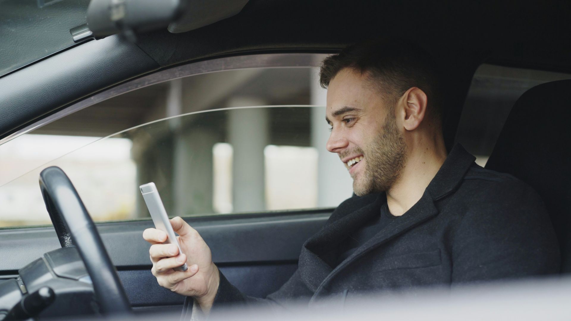 Man smiling while looking at his phone in car