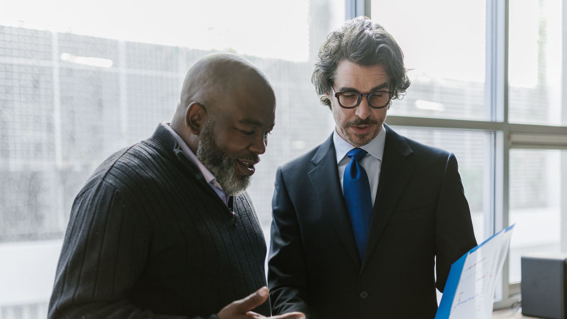 Two businessmen discussing and reviewing documents in a modern office setting.