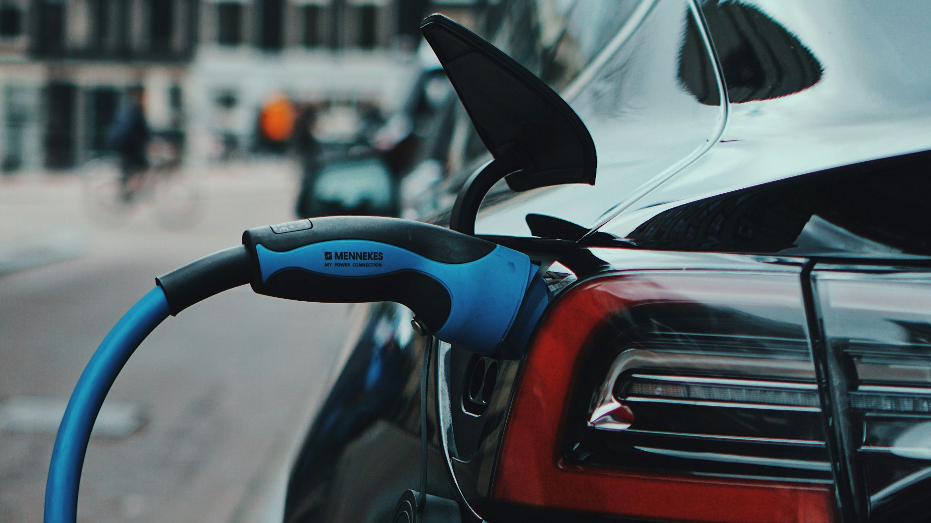 A black electric car charging on a city street with a blue cable