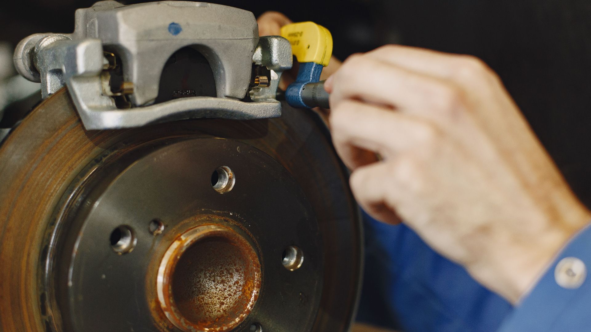 Mechanic working on car disc brake, inspecting for wear and maintenance.