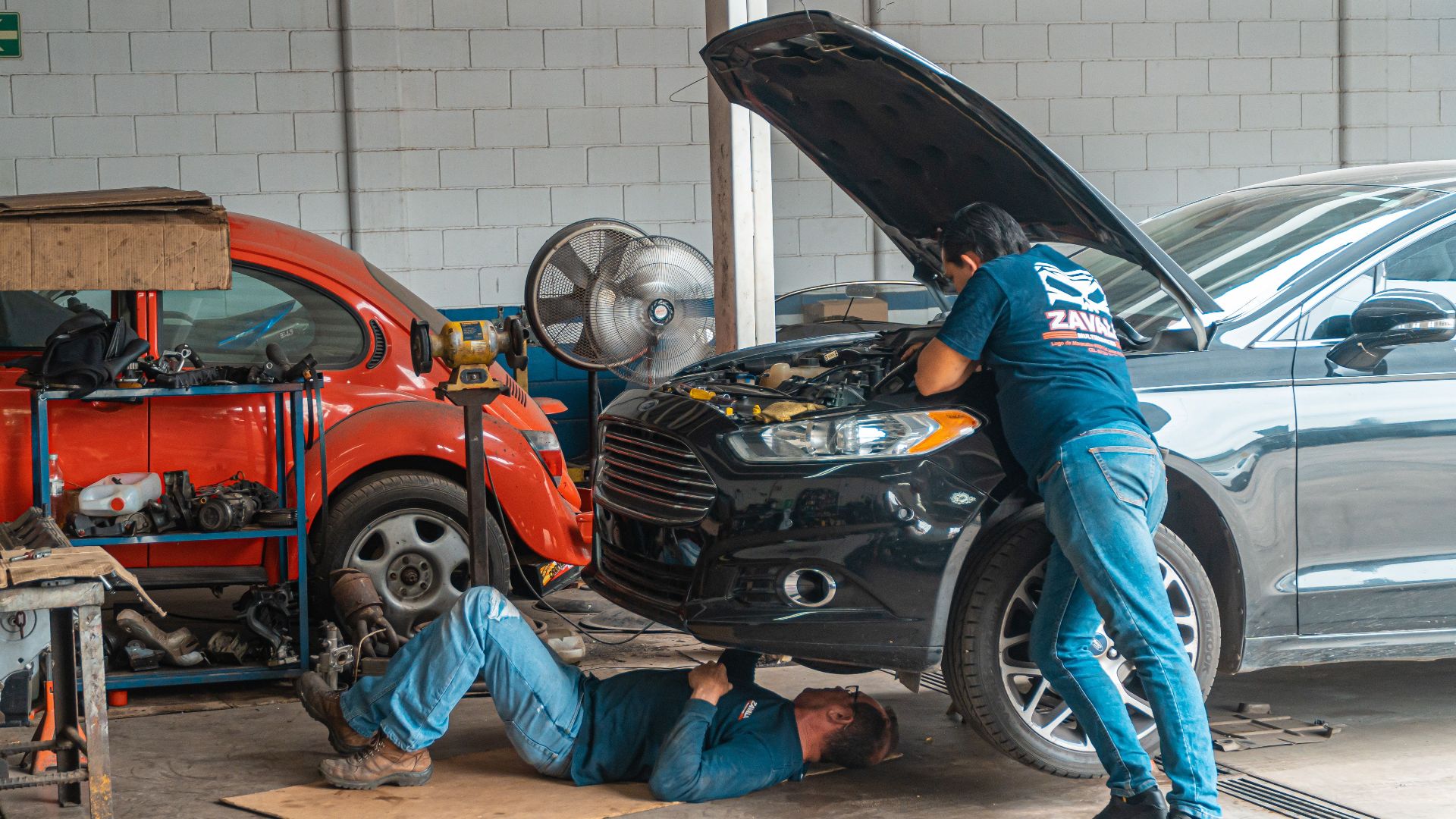 Mechanics working in an automotive workshop, repairing cars and performing maintenance.