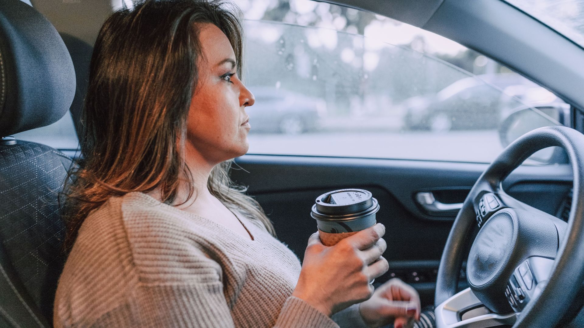 A woman in a car holding a disposable coffee cup, showing focus.