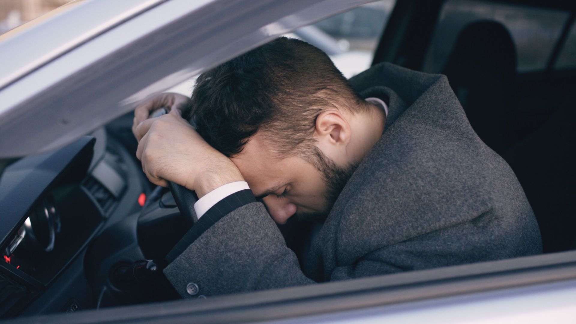 Man in car showing stress with head on steering wheel, highlighting emotional fatigue.