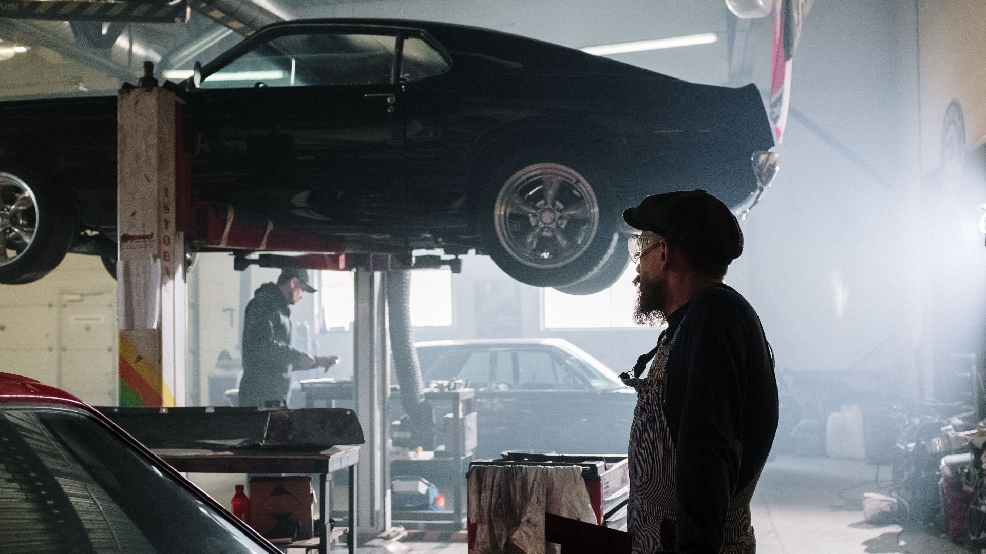 Mechanics busy at work in a dimly lit auto repair garage with a raised car.