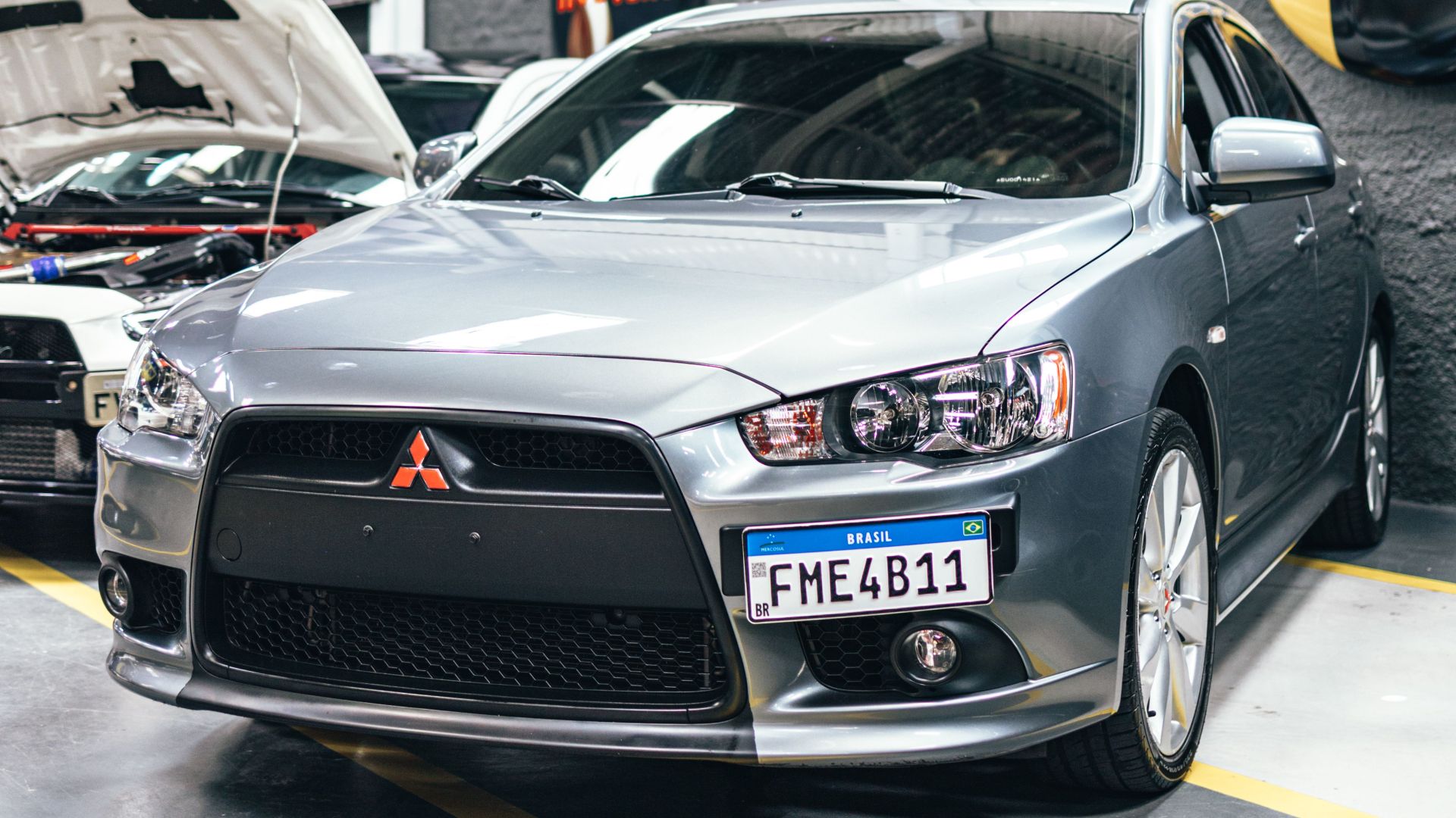 Gray Mitsubishi Lancer parked in a workshop with visible license plate and interior details.