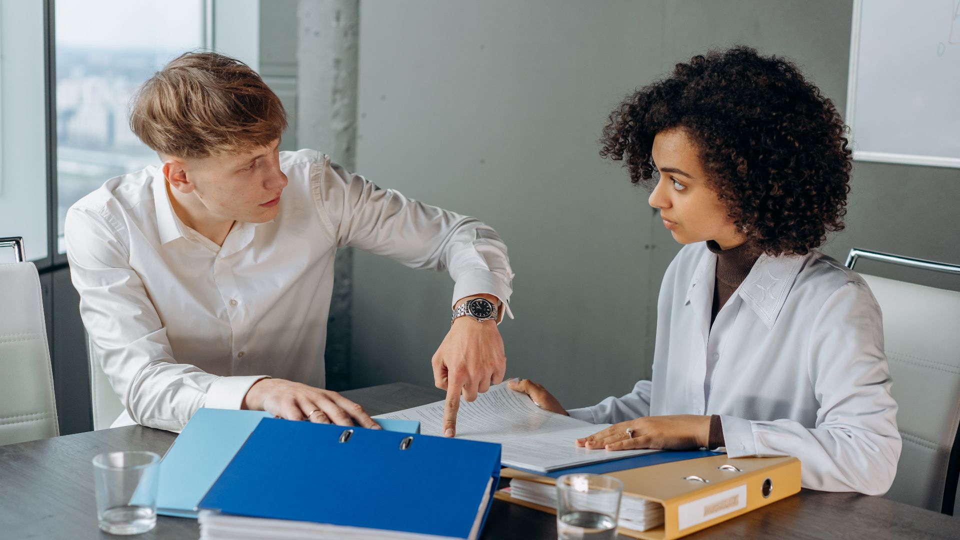 Professional workplace discussion between colleagues reviewing documents at an office table.