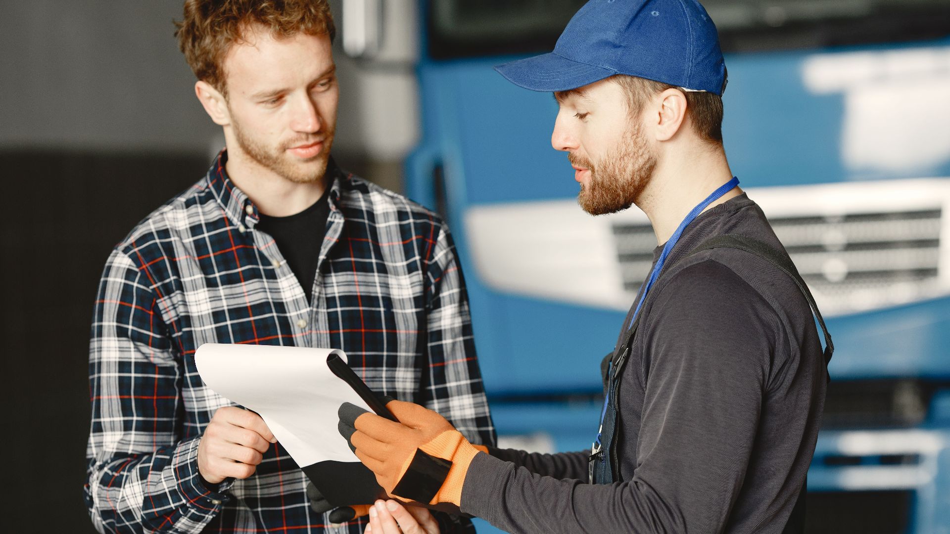 Mechanic in uniform talks with a customer about vehicle maintenance inside a garage.