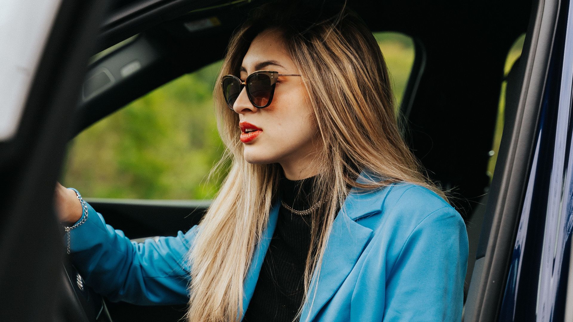 Elegant woman in blue blazer and sunglasses driving a new car in Curitiba, Brazil.