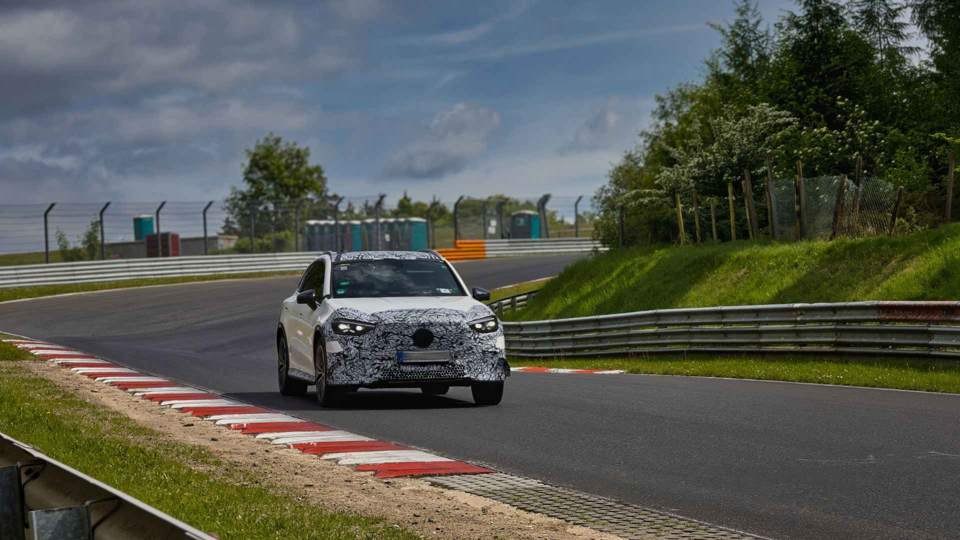 Camouflaged sports car driving on the iconic Nurburgring race track.