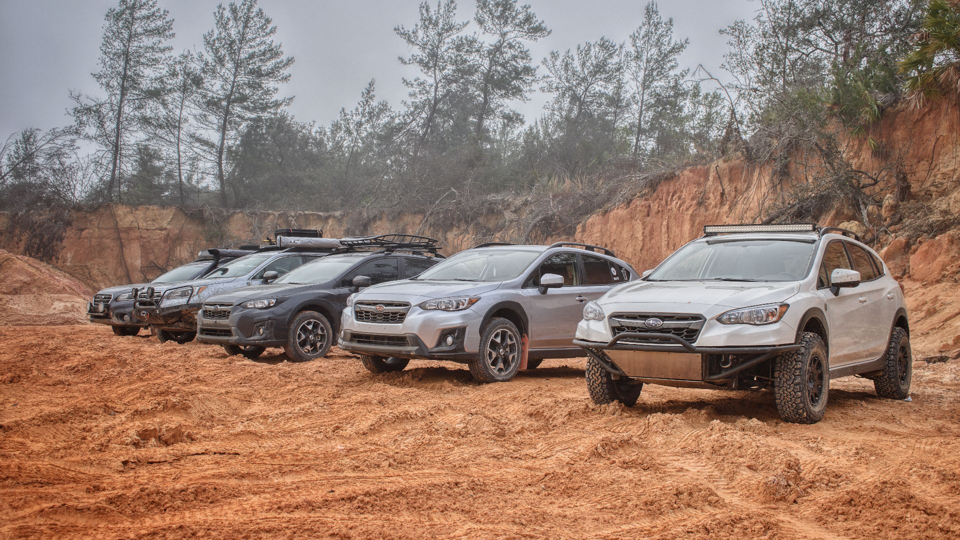 A row of SUVs parked on rough, dusty terrain with trees and a clay backdrop, showcasing adventure and ruggedness.