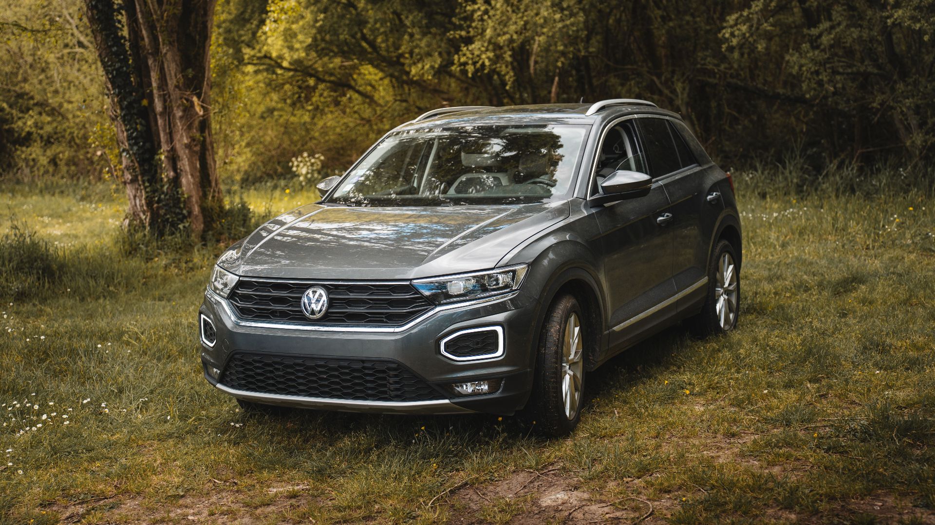 A modern Volkswagen T-Roc SUV parked in a picturesque forest meadow on a sunny day.