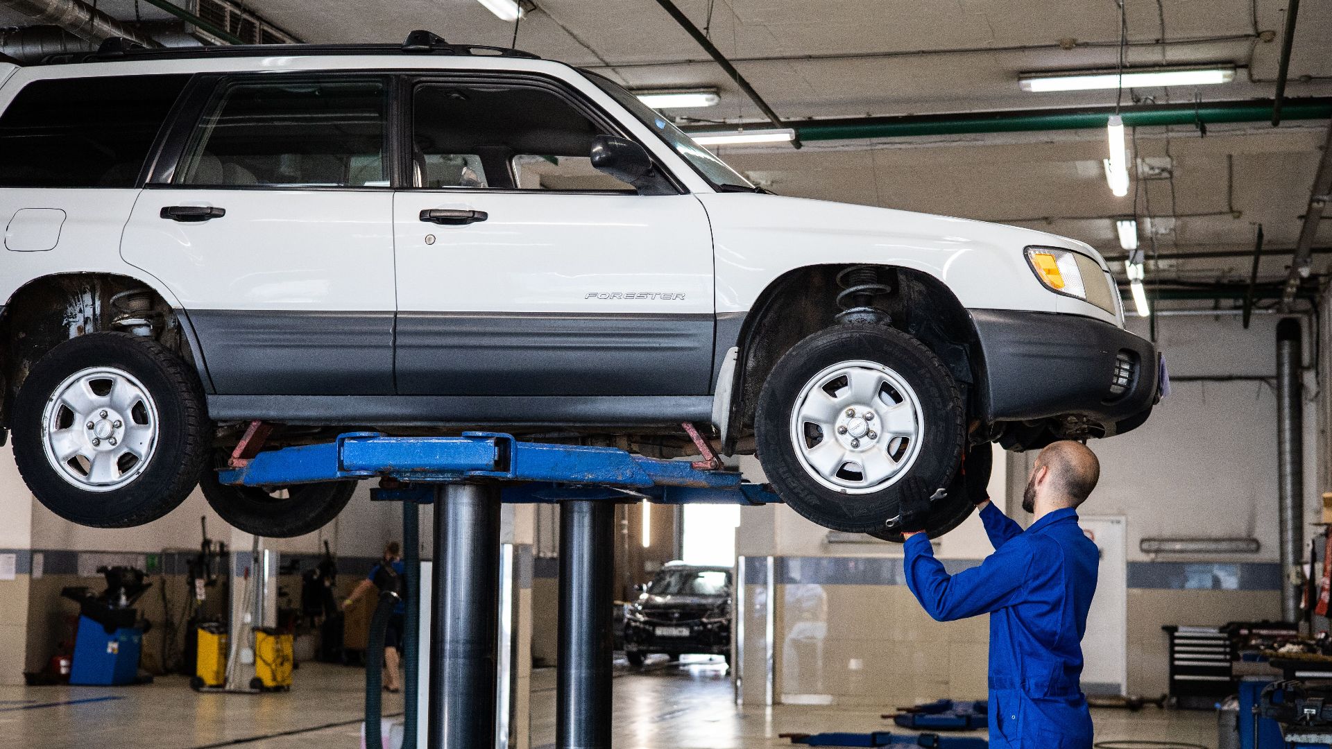 A mechanic inspecting a white SUV lifted in a well-lit auto repair shop.