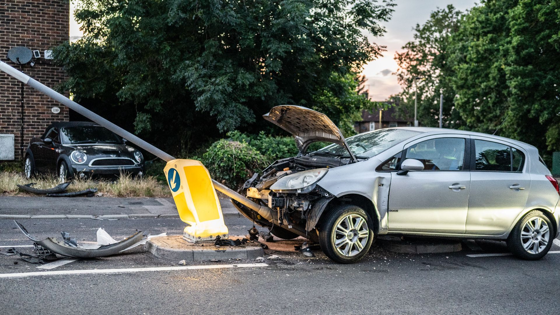 A damaged car that crashed into a lamp post on a London street during twilight.