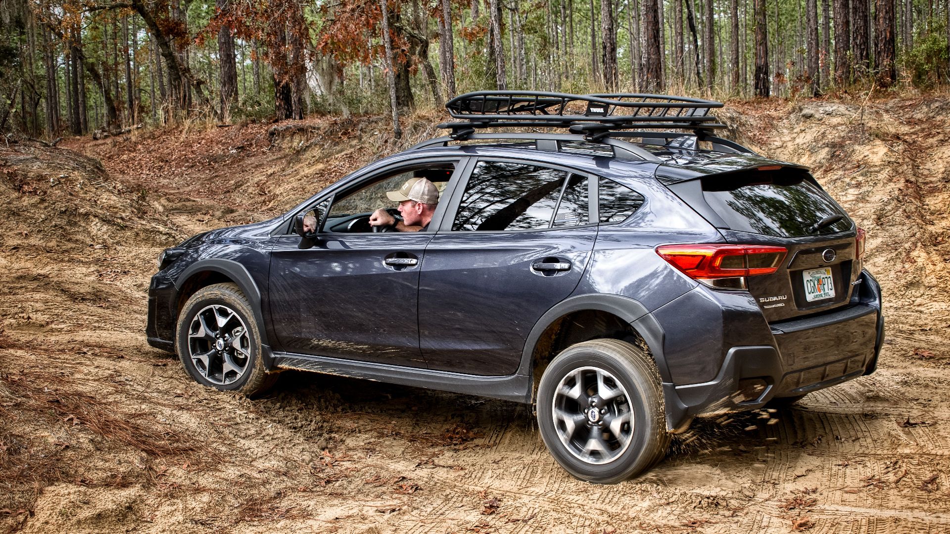 A man driving a Subaru on a rugged dirt road through a forest, showcasing off-road capabilities.