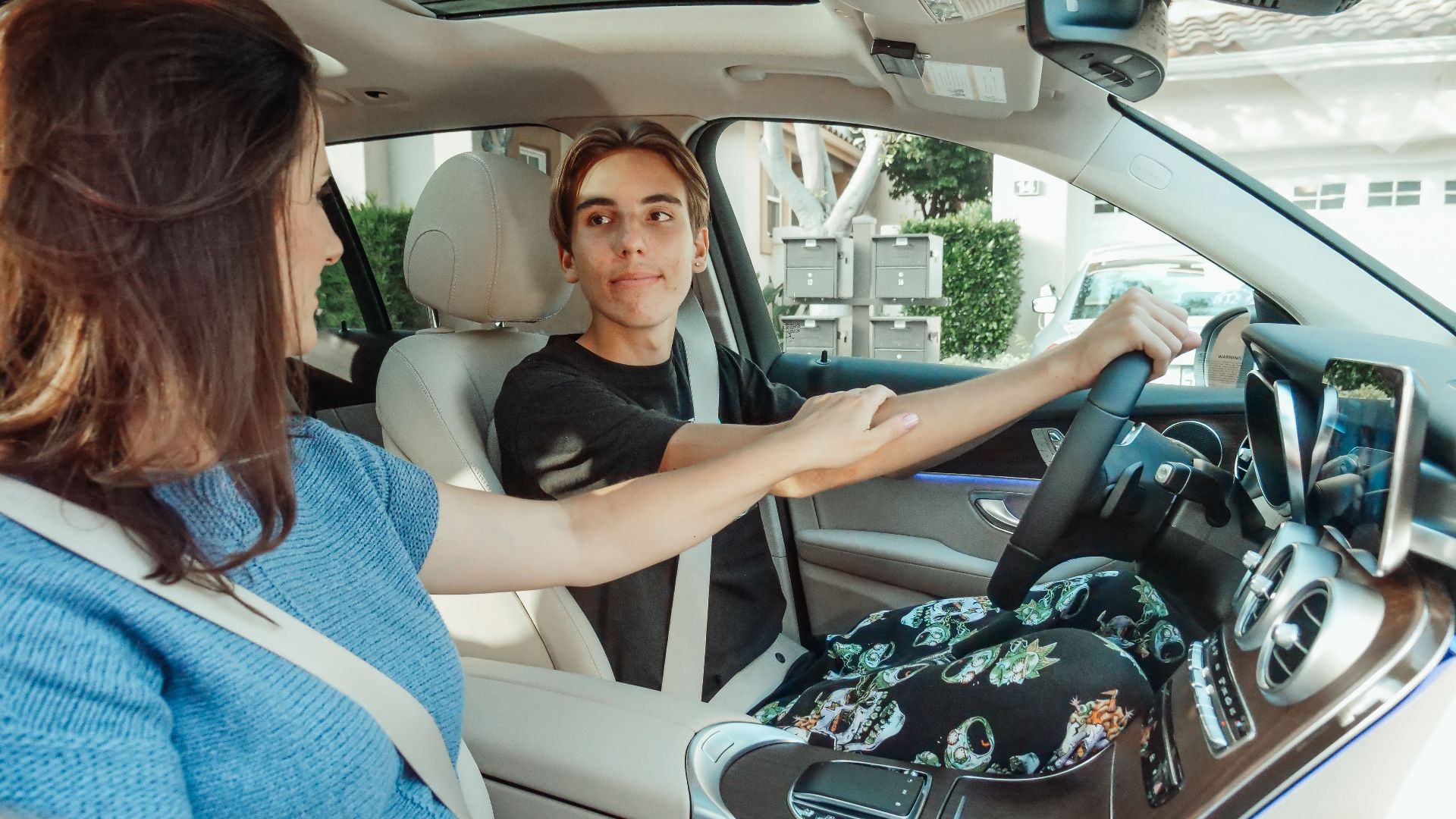 A mother supports her teenage son as he learns to drive in a car