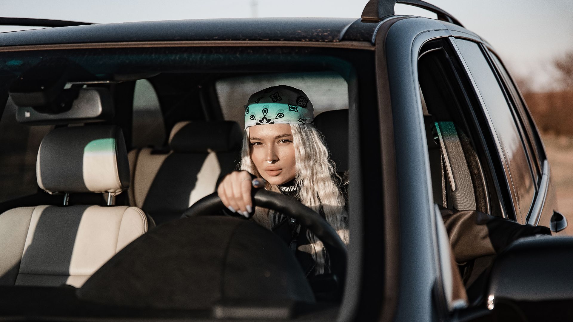 A woman driving an SUV, wearing a bandana, looking confidently ahead on a sunny day.