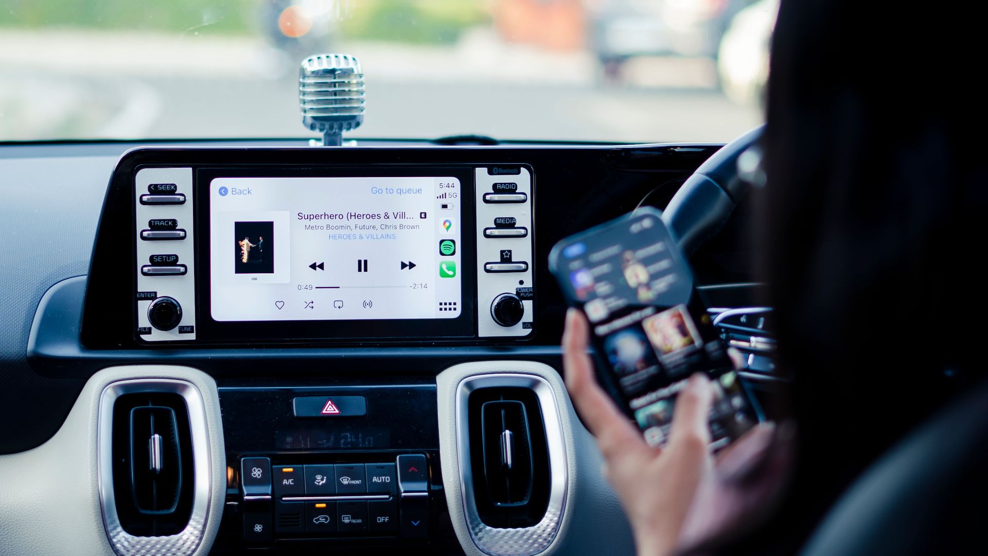 Car dashboard with a touchscreen display and person using a smartphone inside a vehicle.