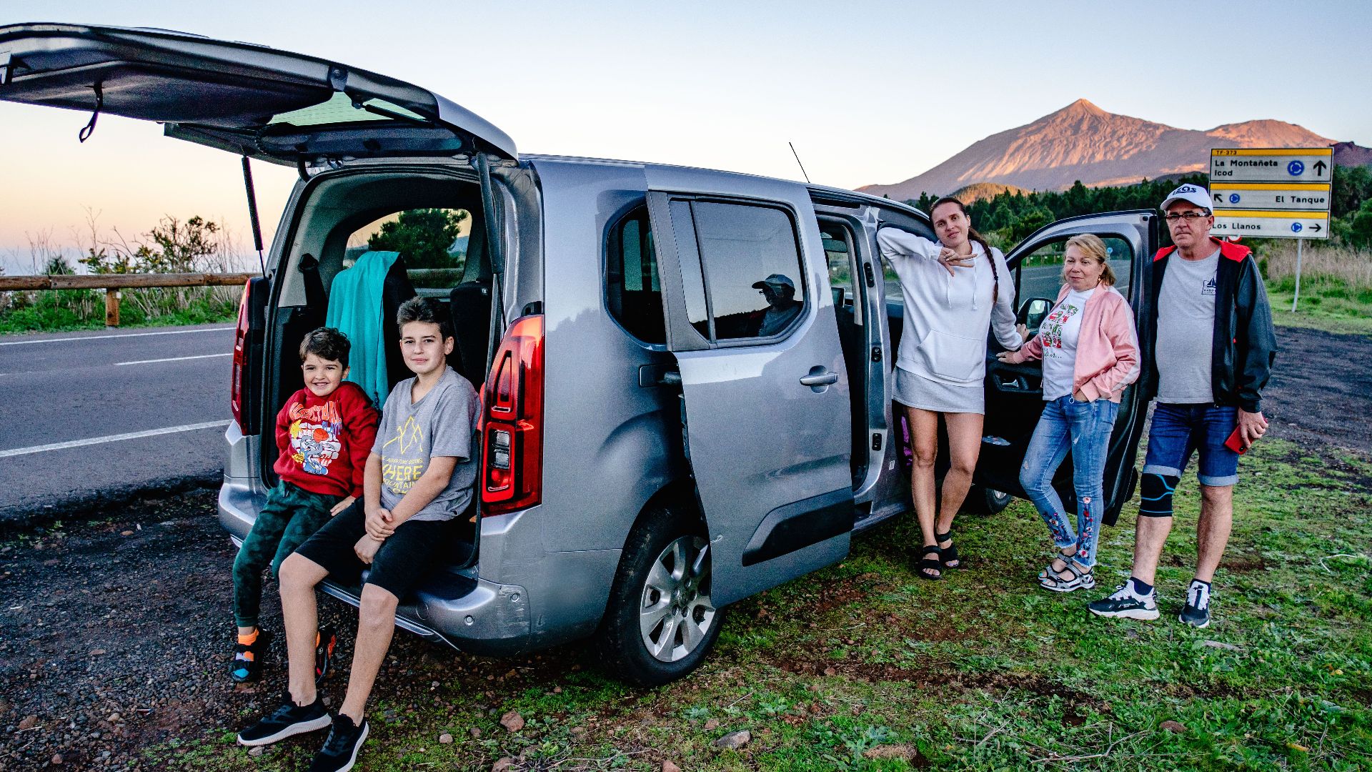 A family enjoys a scenic road trip by Mount Teide, Spain, with a van parked by the roadside.