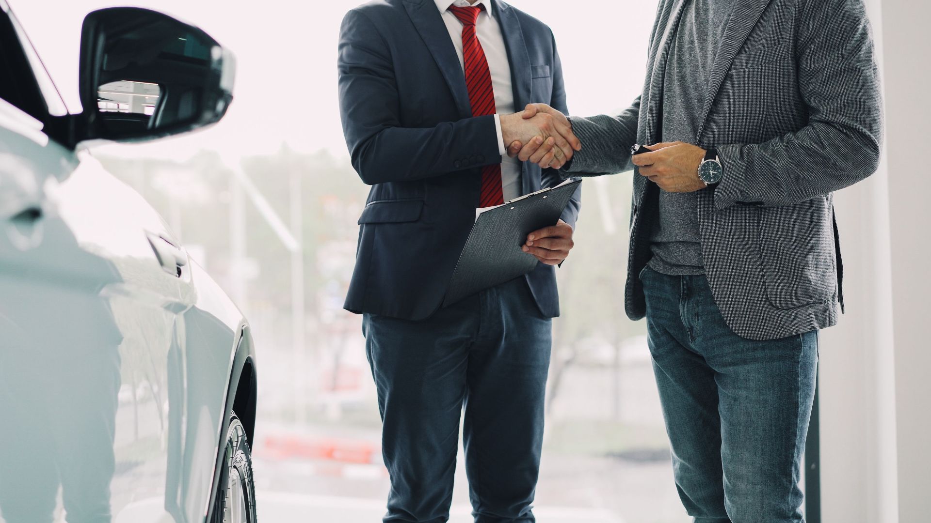 Two men shaking hands in a car dealership, symbolizing a successful business deal.