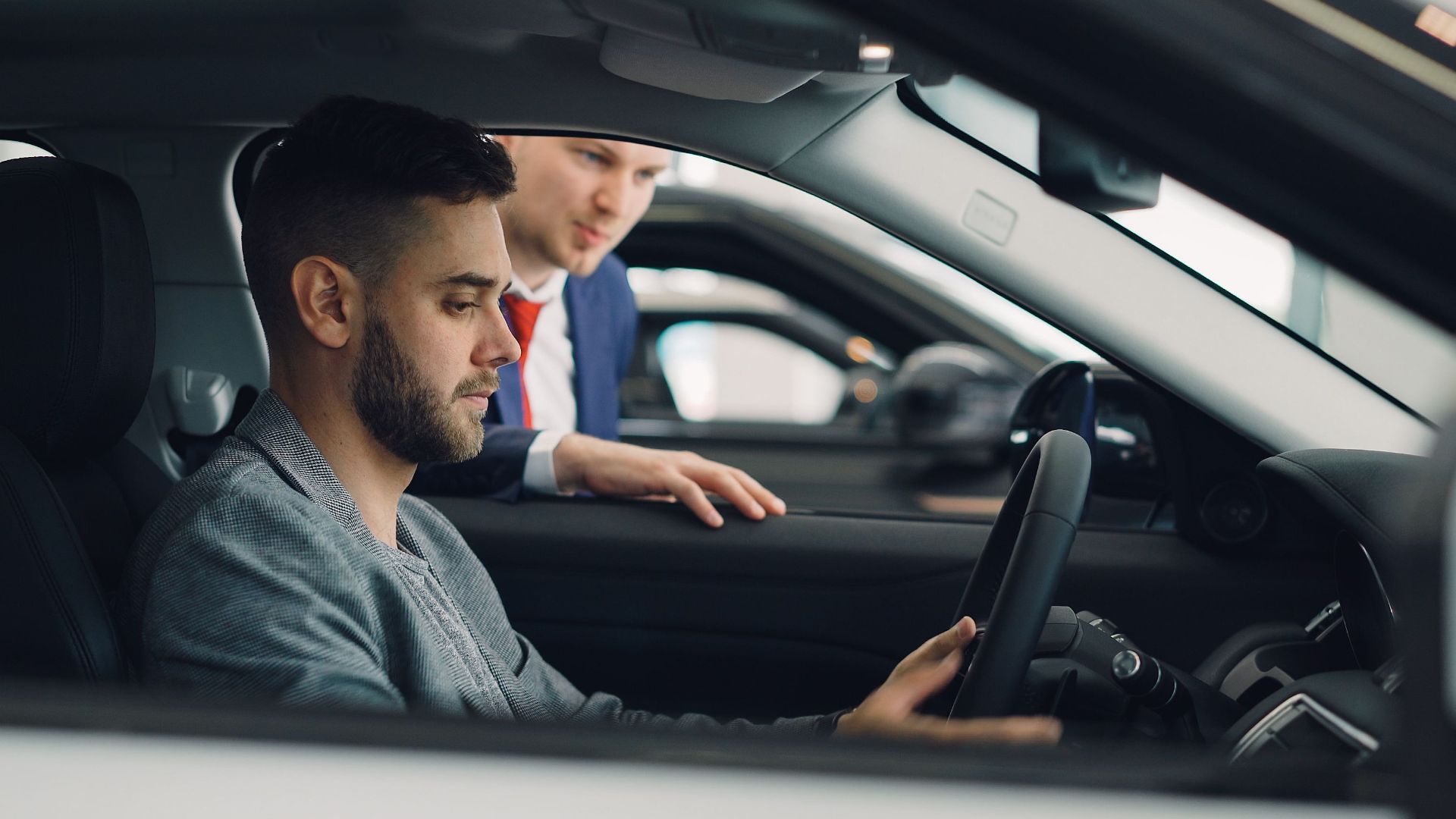 Man examining car interior with salesman at a dealership, highlighting car features.