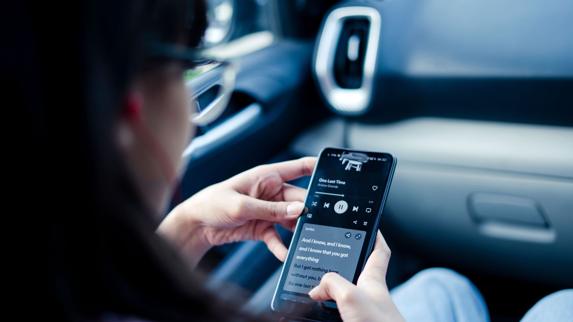 Woman using smartphone to listen to music in a car, focusing on lyrics.