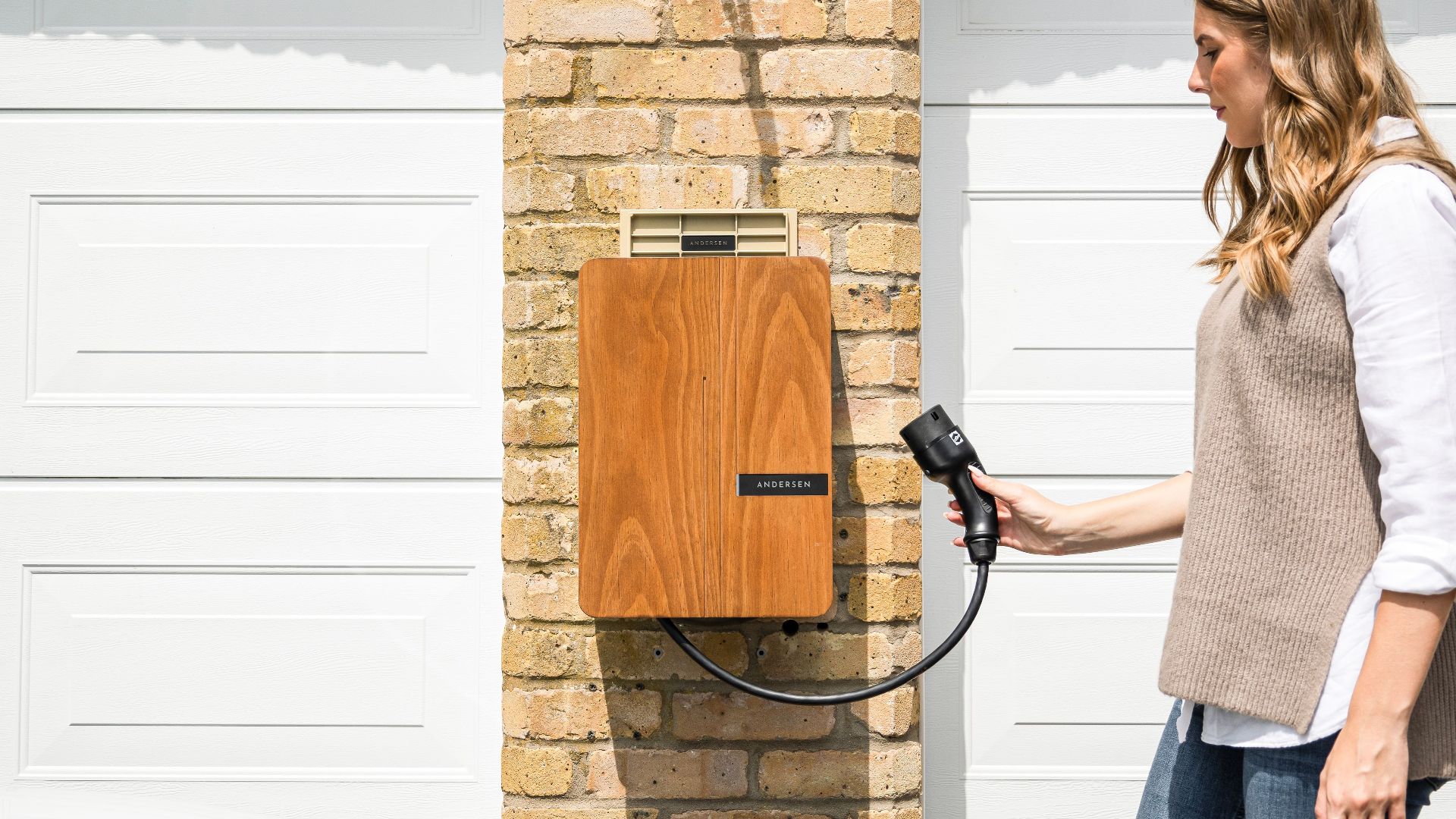 A woman uses a home electric vehicle charger mounted on a brick wall.