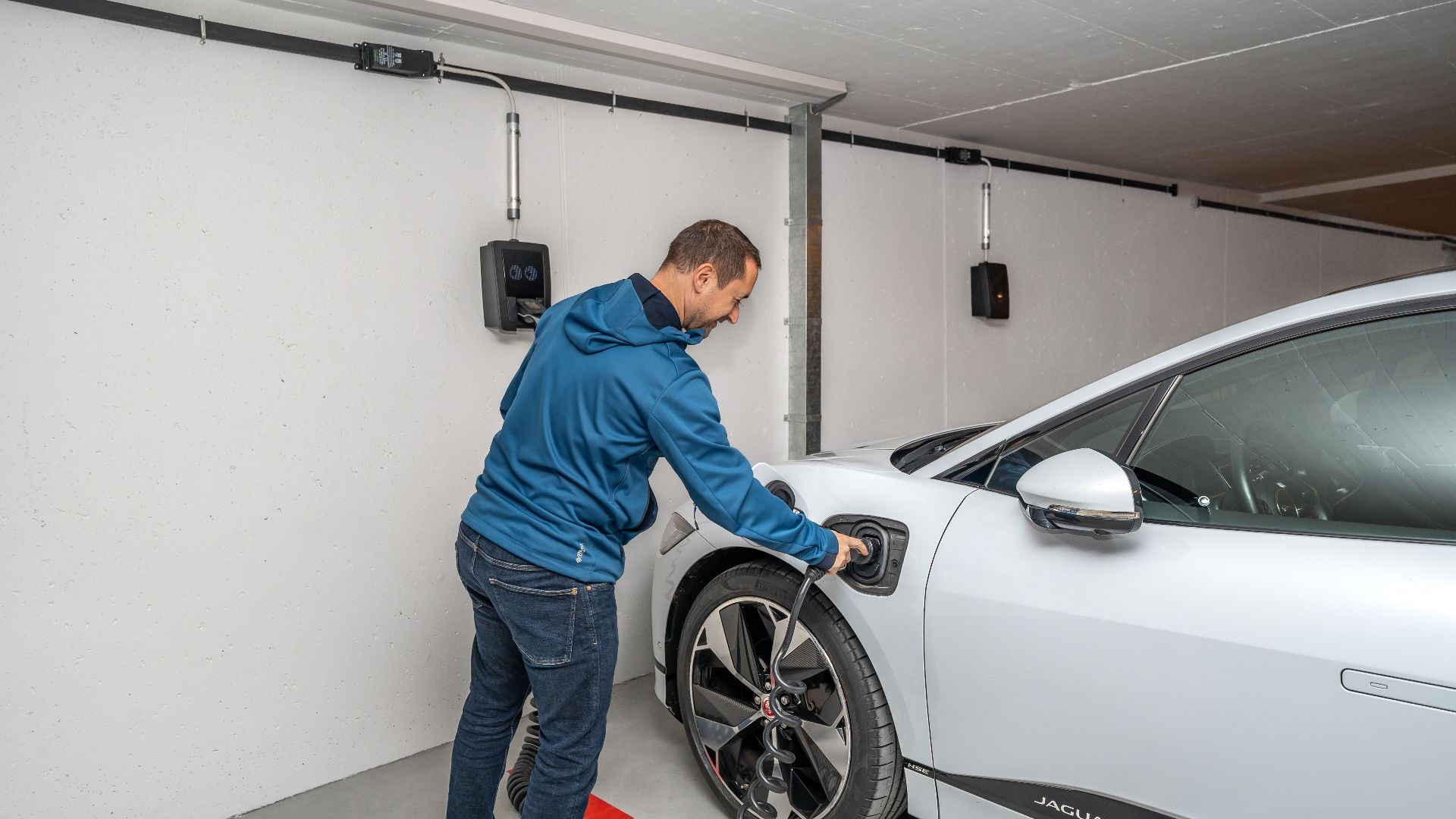 A man connects an electric car to a charging station in a modern indoor garage setting.