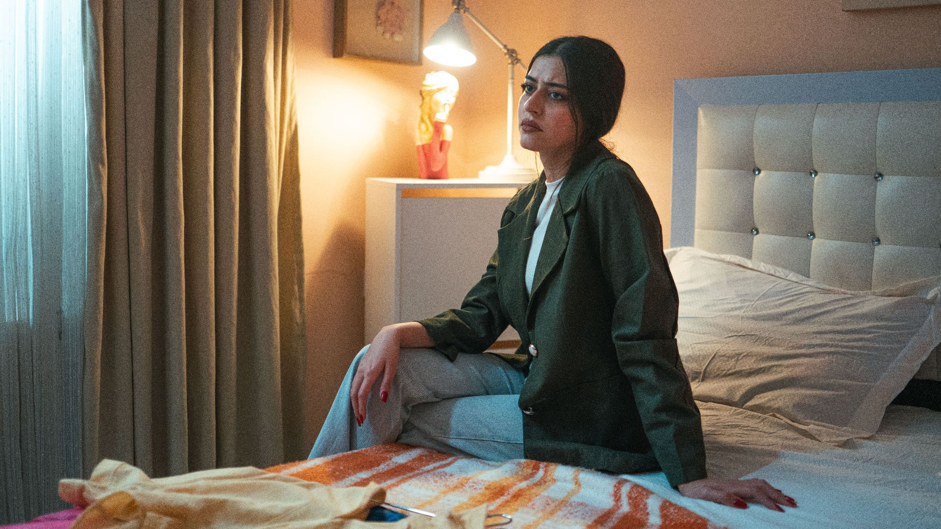 A thoughtful woman sits on a bed, bathed in warm light, conveying introspection.