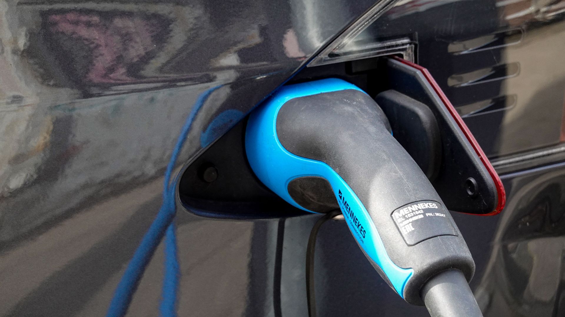 Close-up of an electric vehicle being charged using a Mennekes EV connector.