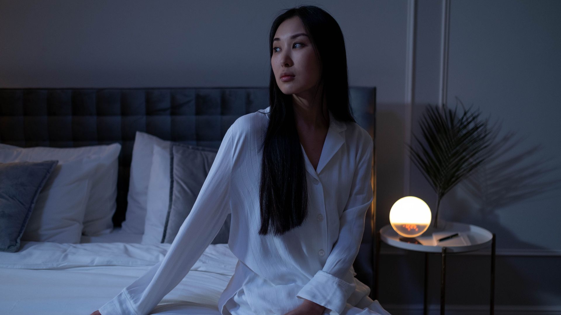 Woman in white pajamas sitting on a bed with warm lighting, showcasing a calm evening indoors.
