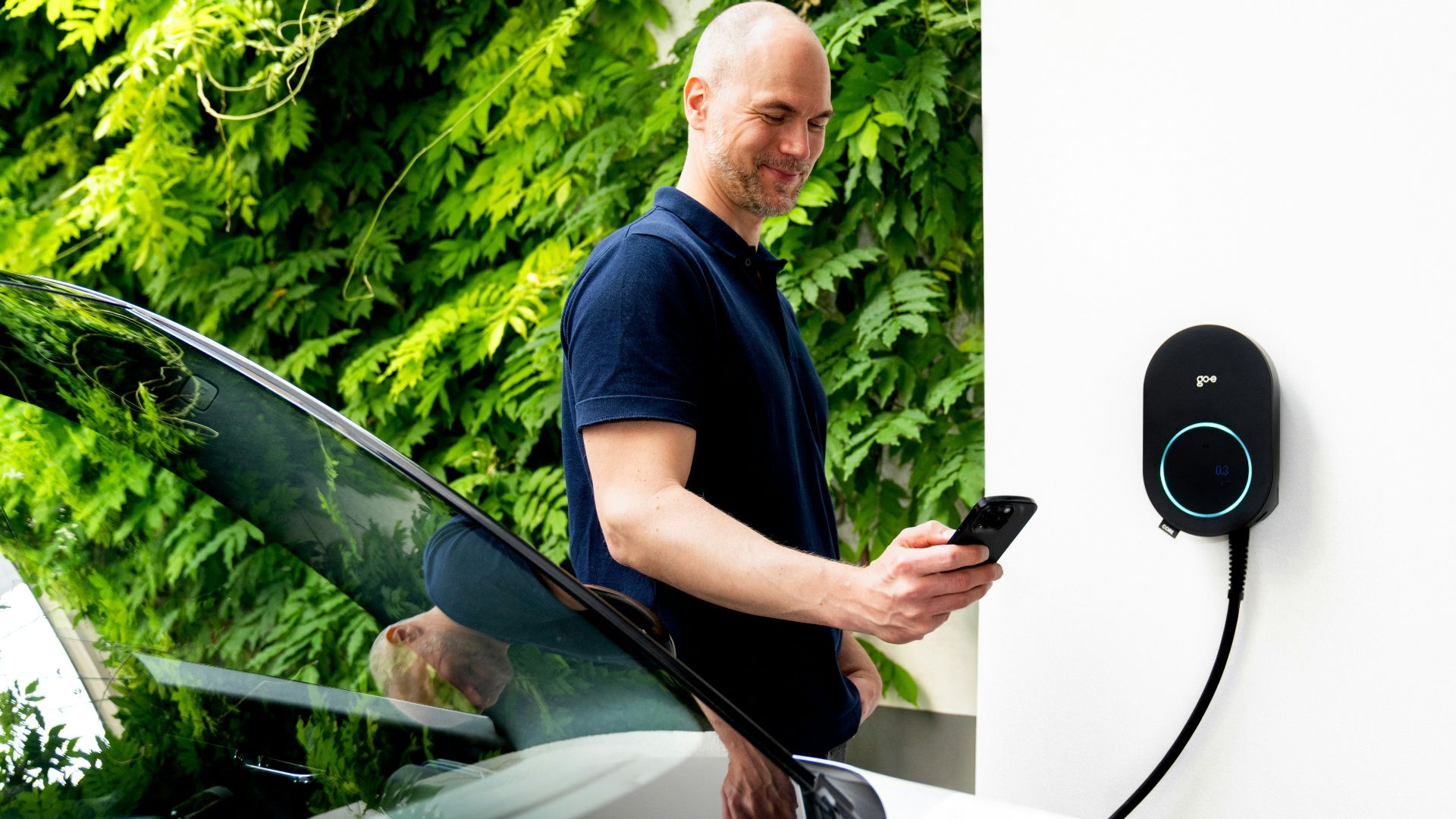 Man using phone near electric car charging station