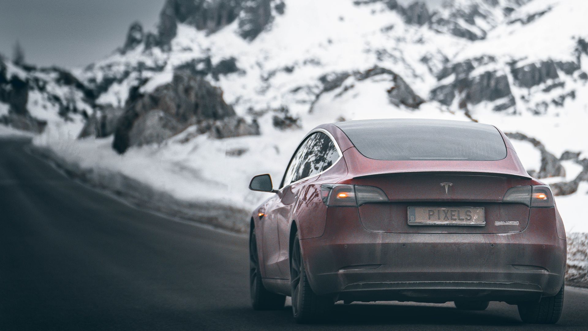 Red electric car driving through a scenic snowy mountain landscape in winter.