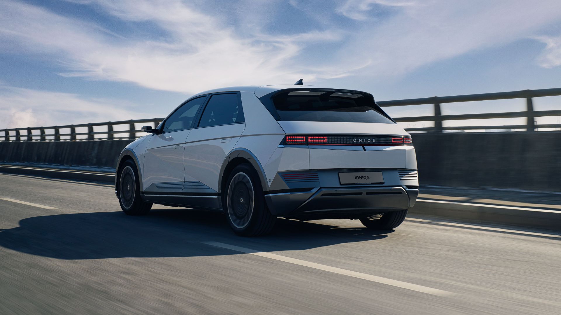 Sleek white electric car driving on an open highway under a bright blue sky.