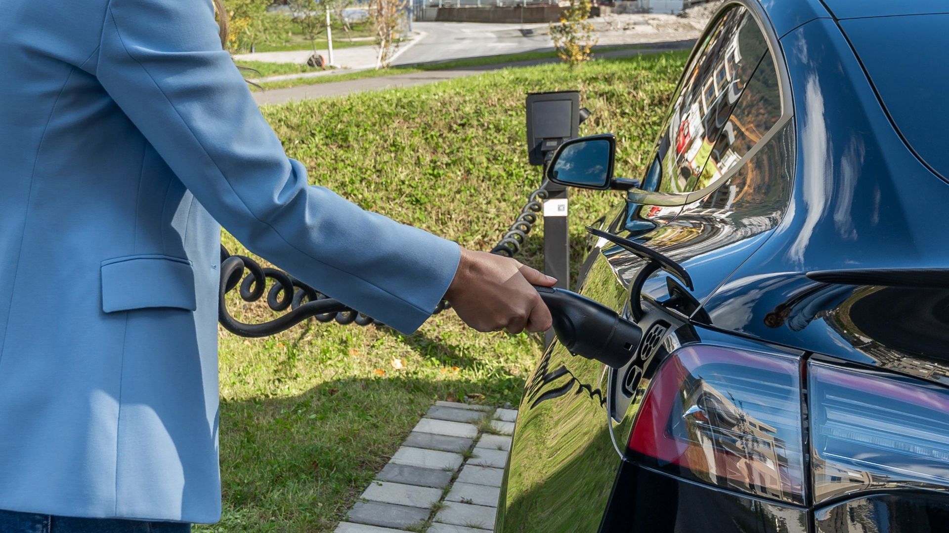Person connecting an electric car to a charging station outdoors, showcasing green energy transition.