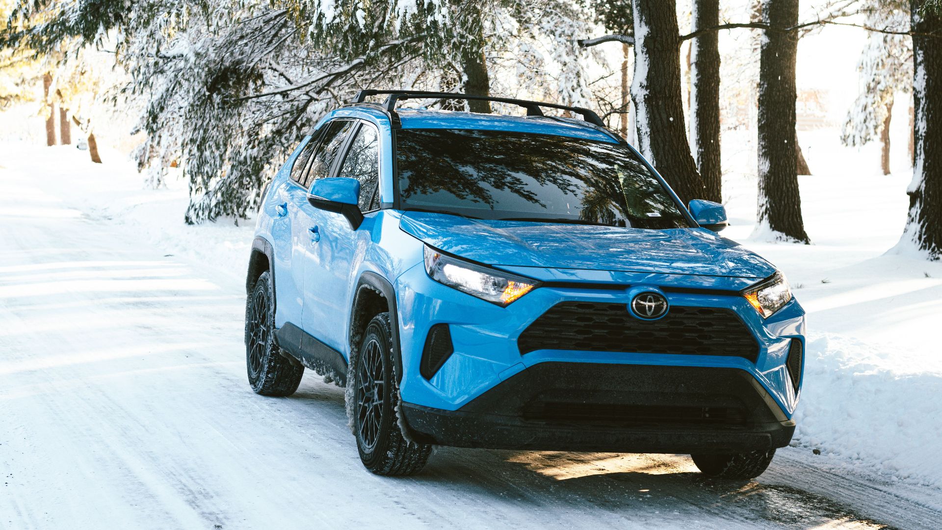 A shiny blue SUV parked on a snow-covered forest road on a bright winter day.