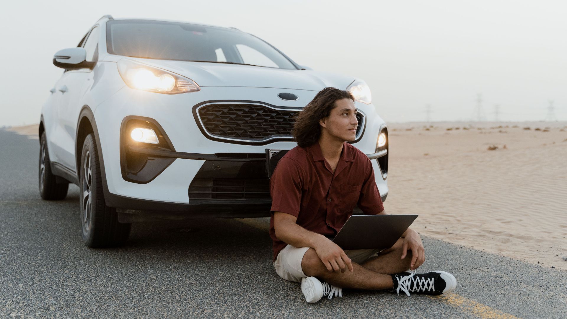 A man with a laptop sitting by an SUV on a desert road, working remotely.