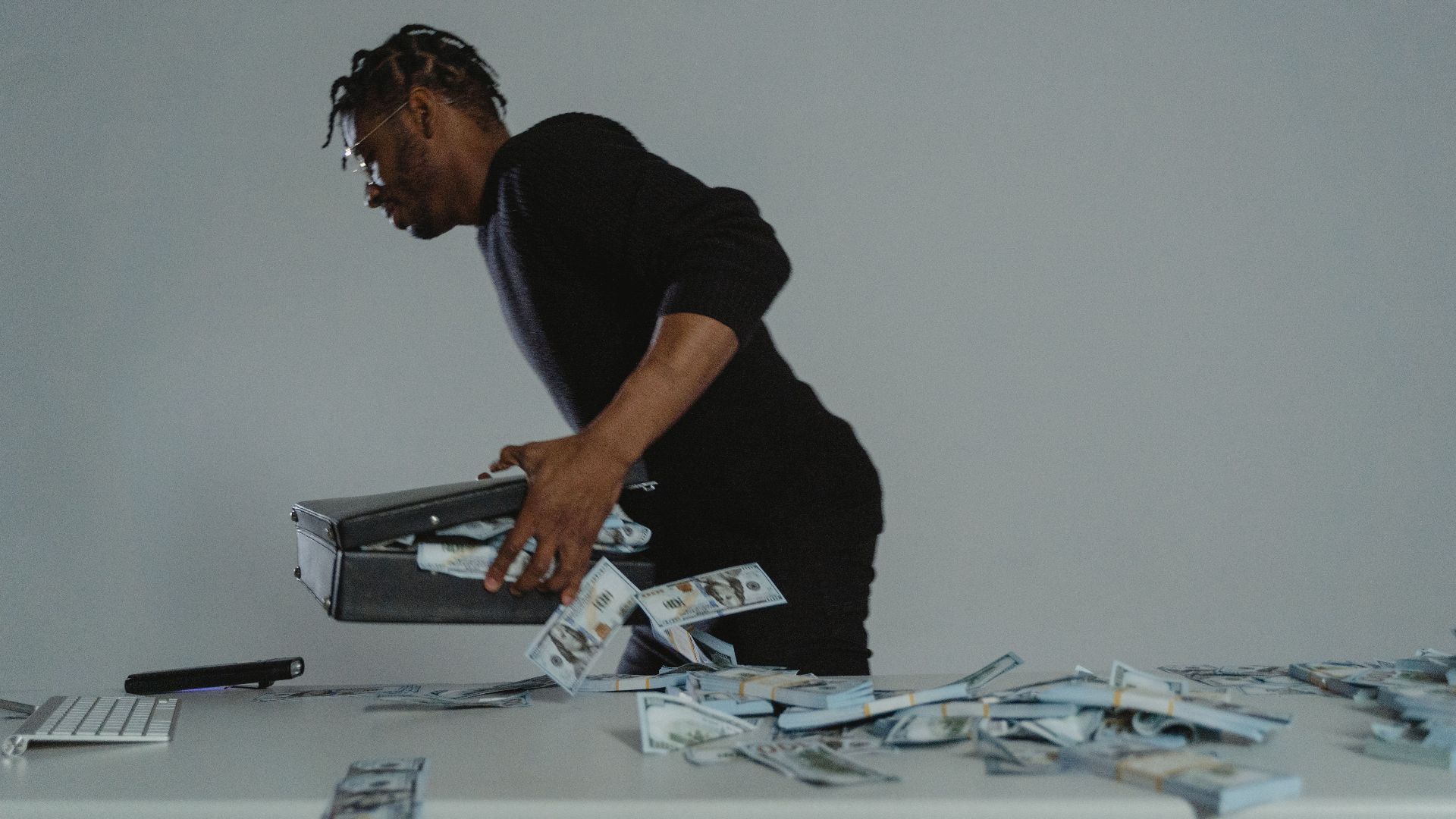 A person quickly gathers cash into a briefcase, conveying a sense of urgency and action.