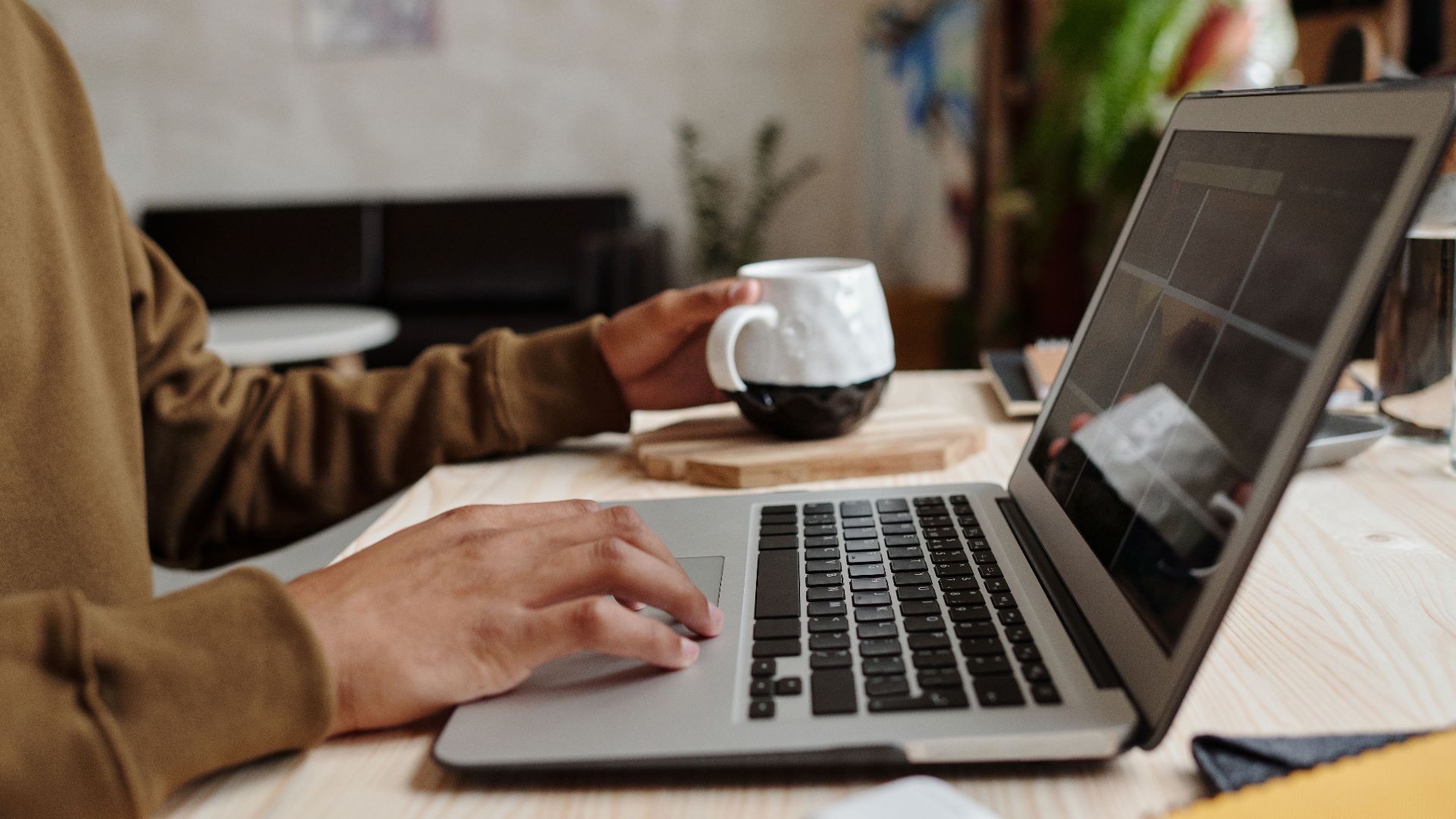 Close-up of a person using a laptop with a coffee mug on a wooden table, ideal for remote work concept.