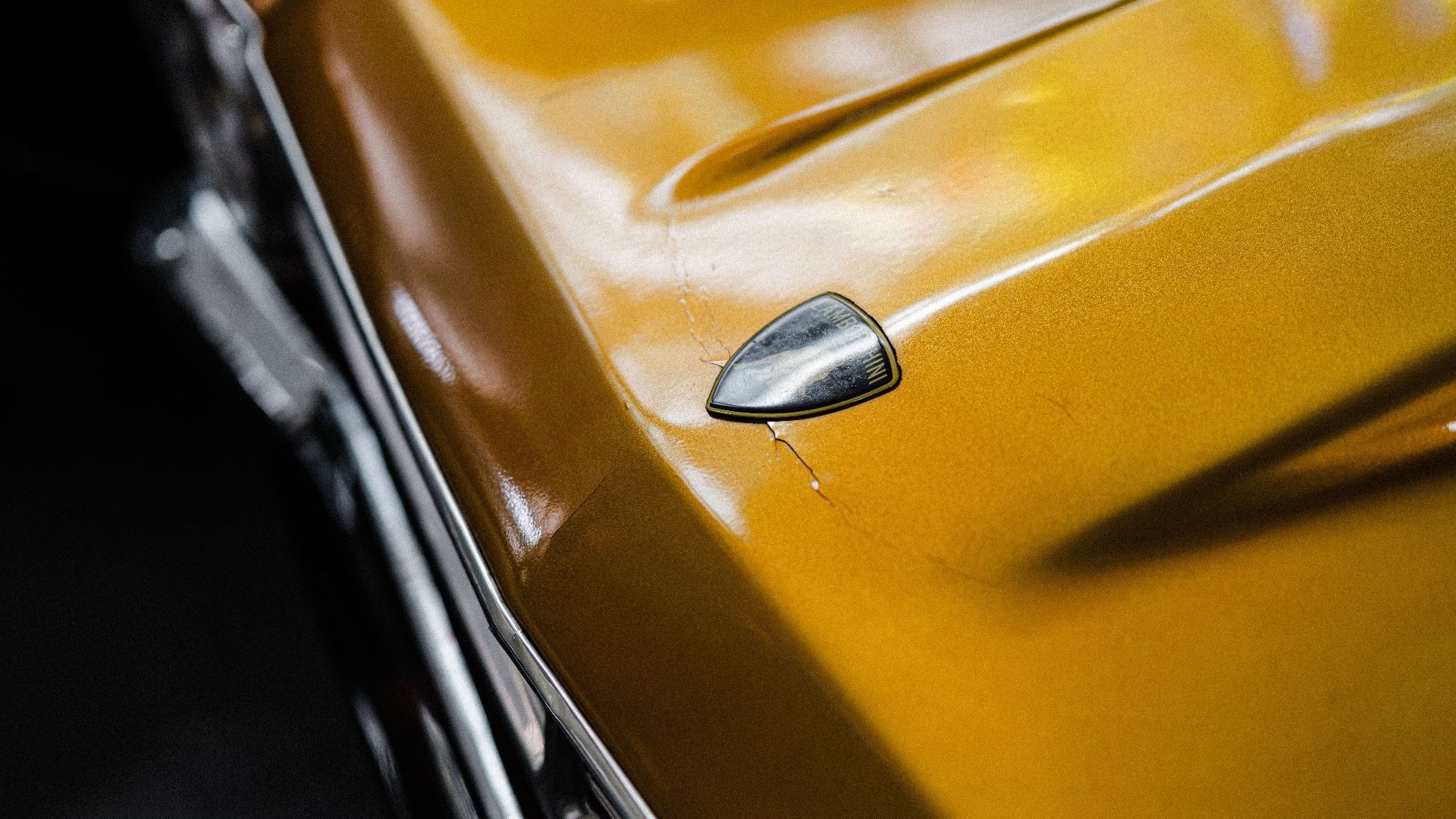 Detailed close-up of a yellow vintage car hood showing small cracks and a chrome accent.