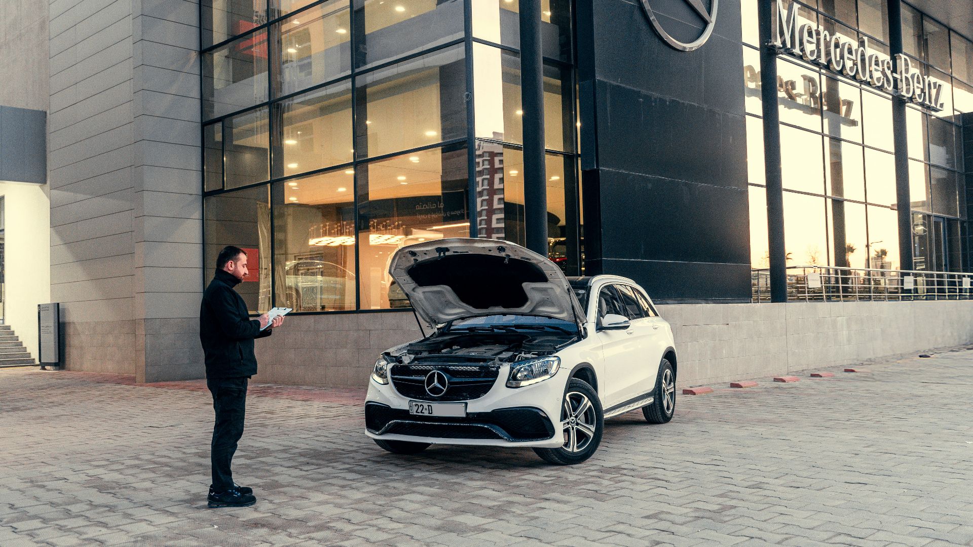 Man looking at car with hood open outside dealership
