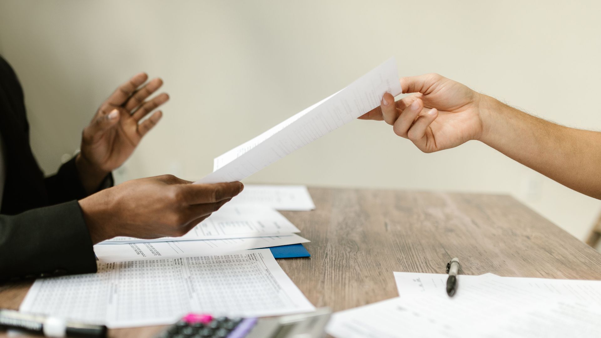 Two professionals exchanging documents in a corporate setting, emphasizing collaboration and paperwork.