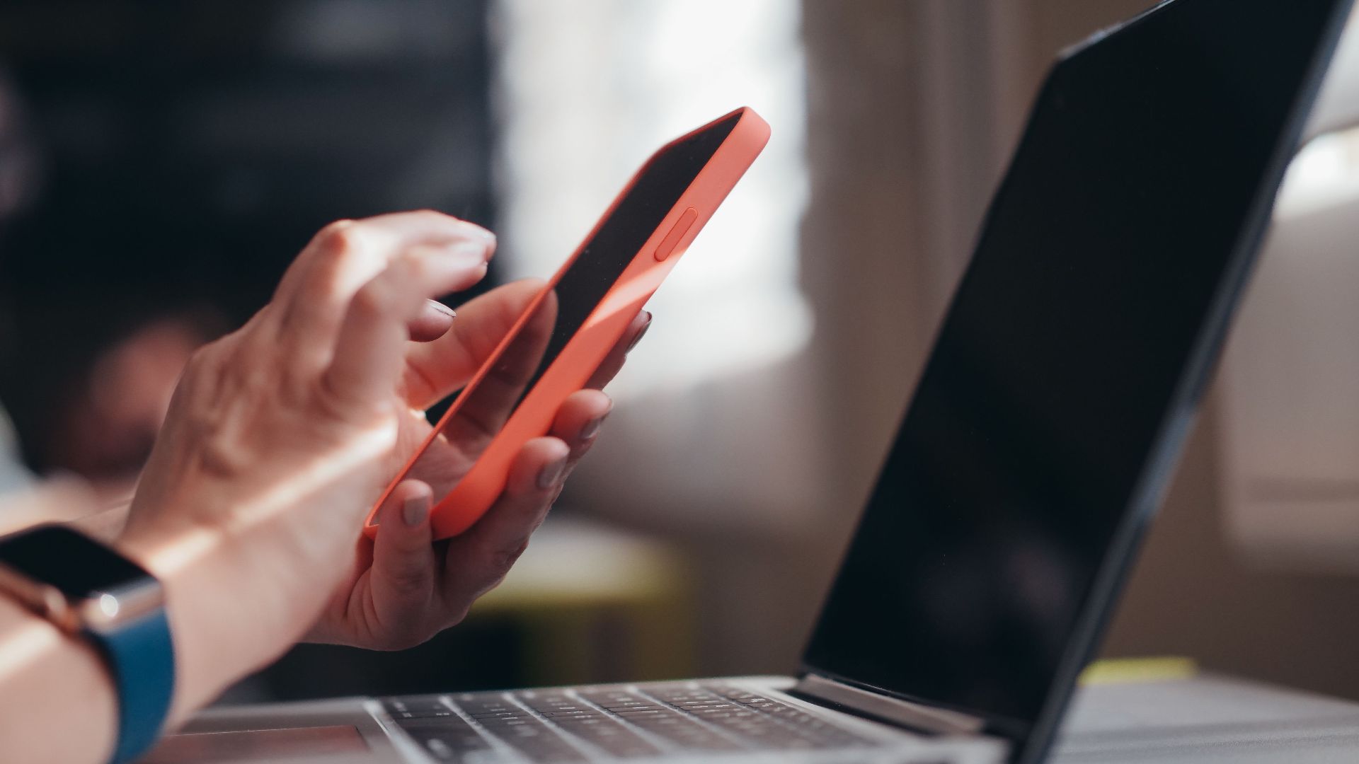 Adult using a smartphone and laptop indoors, showcasing modern technology and multitasking.