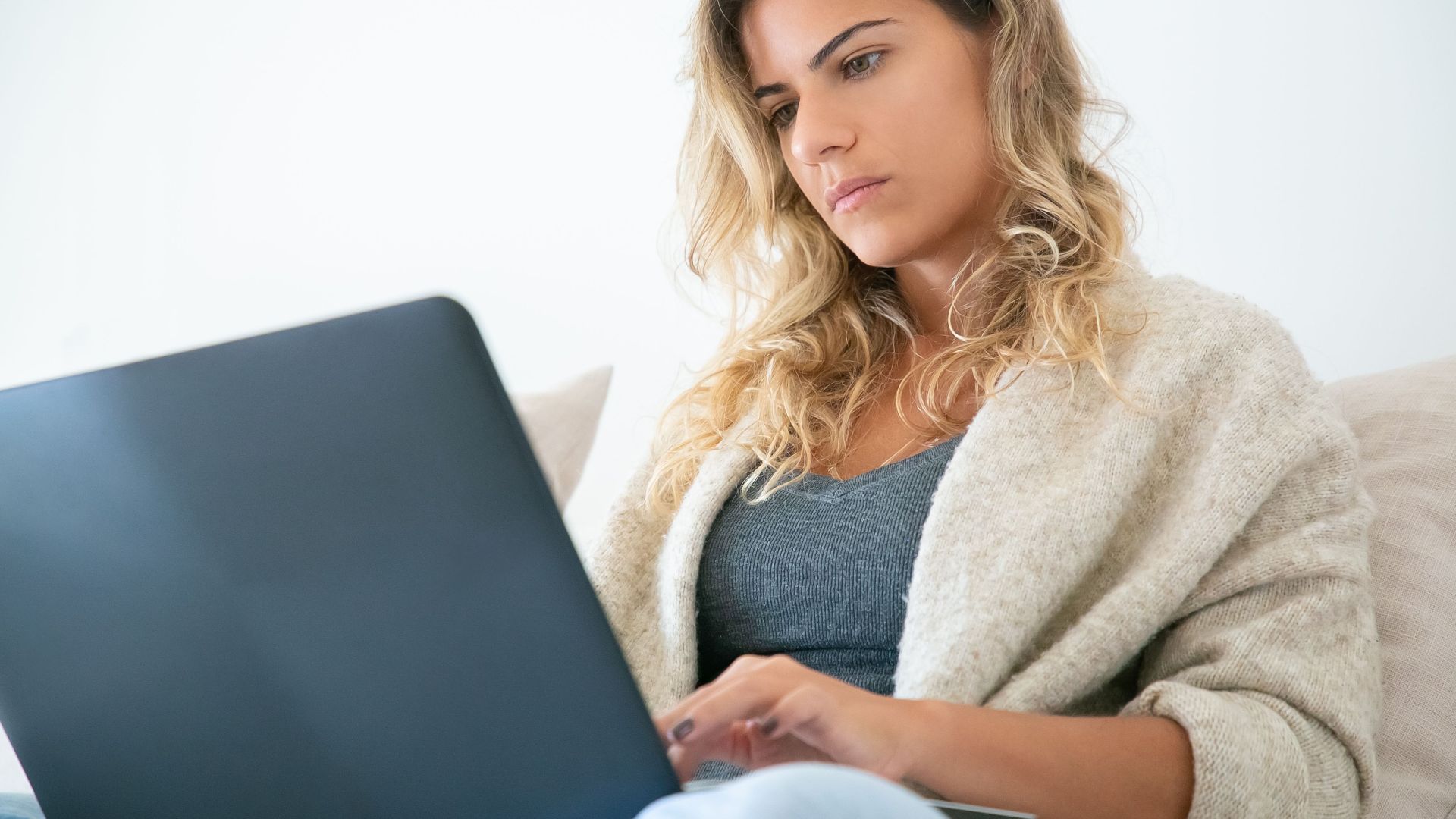 Blonde woman working on a laptop, deeply focused in a cozy home setting.