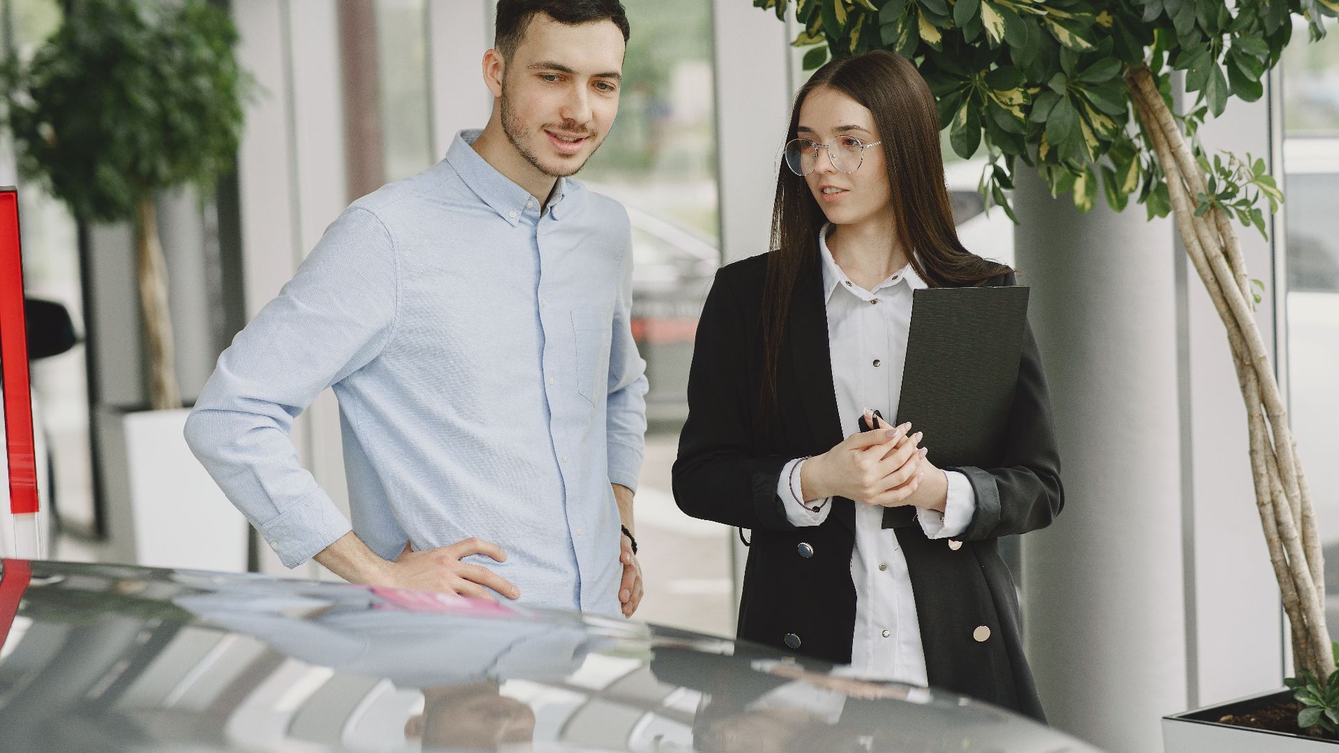 Two professionals discussing business in a modern car showroom with plants around.