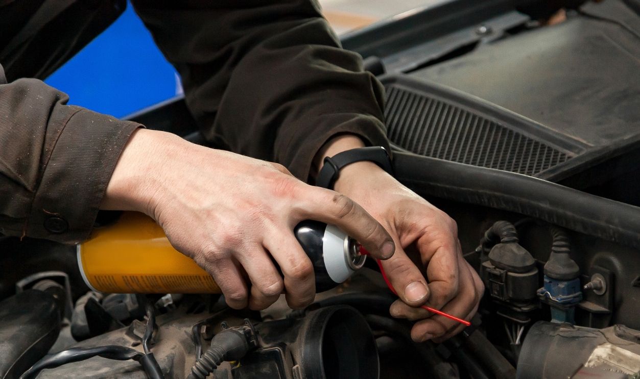 Shutterstock-1589595733, A male mechanic with a can spray gasoline into the intake manifold to start the car during engine breakdown of the ignition and fuel supply system in a vehicle repair workshop. Auto service industry.