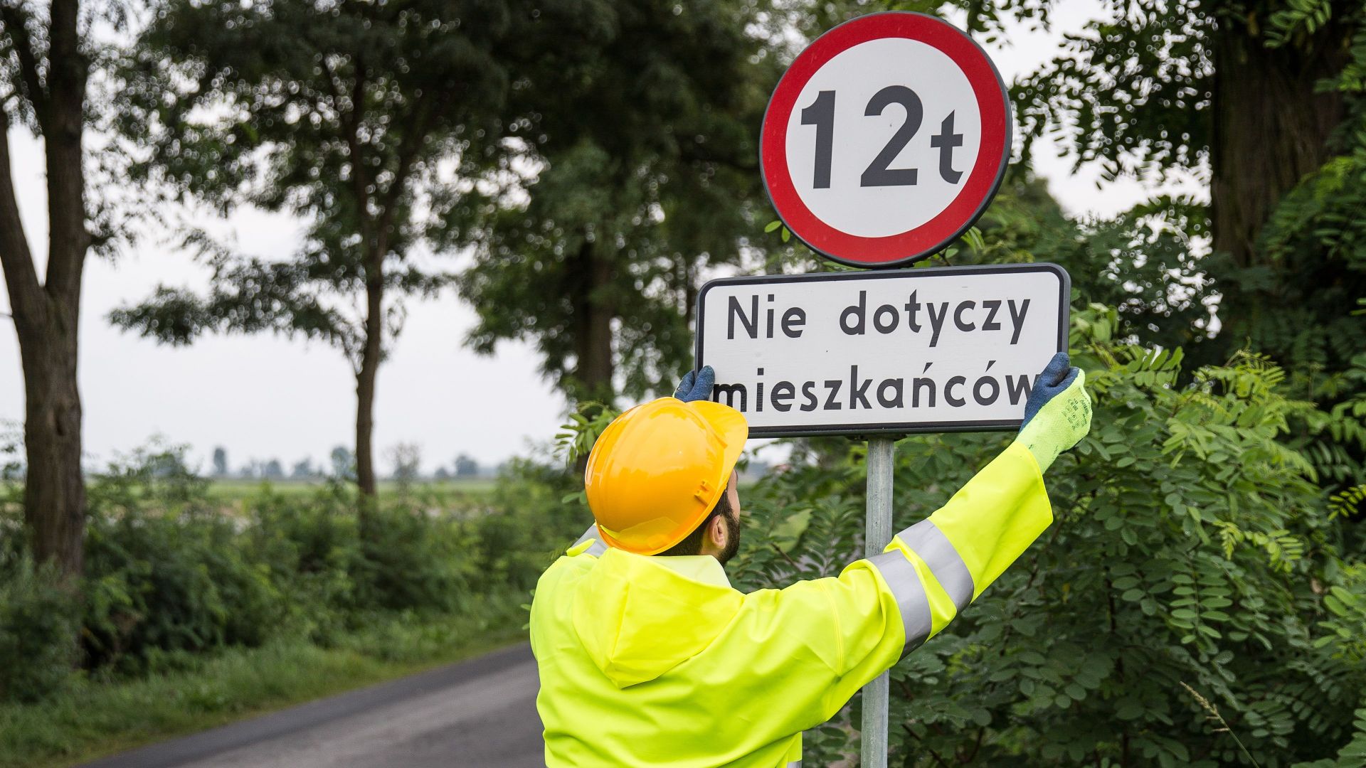 Worker in high-visibility clothing adjusts a road sign on a rural roadwork site.